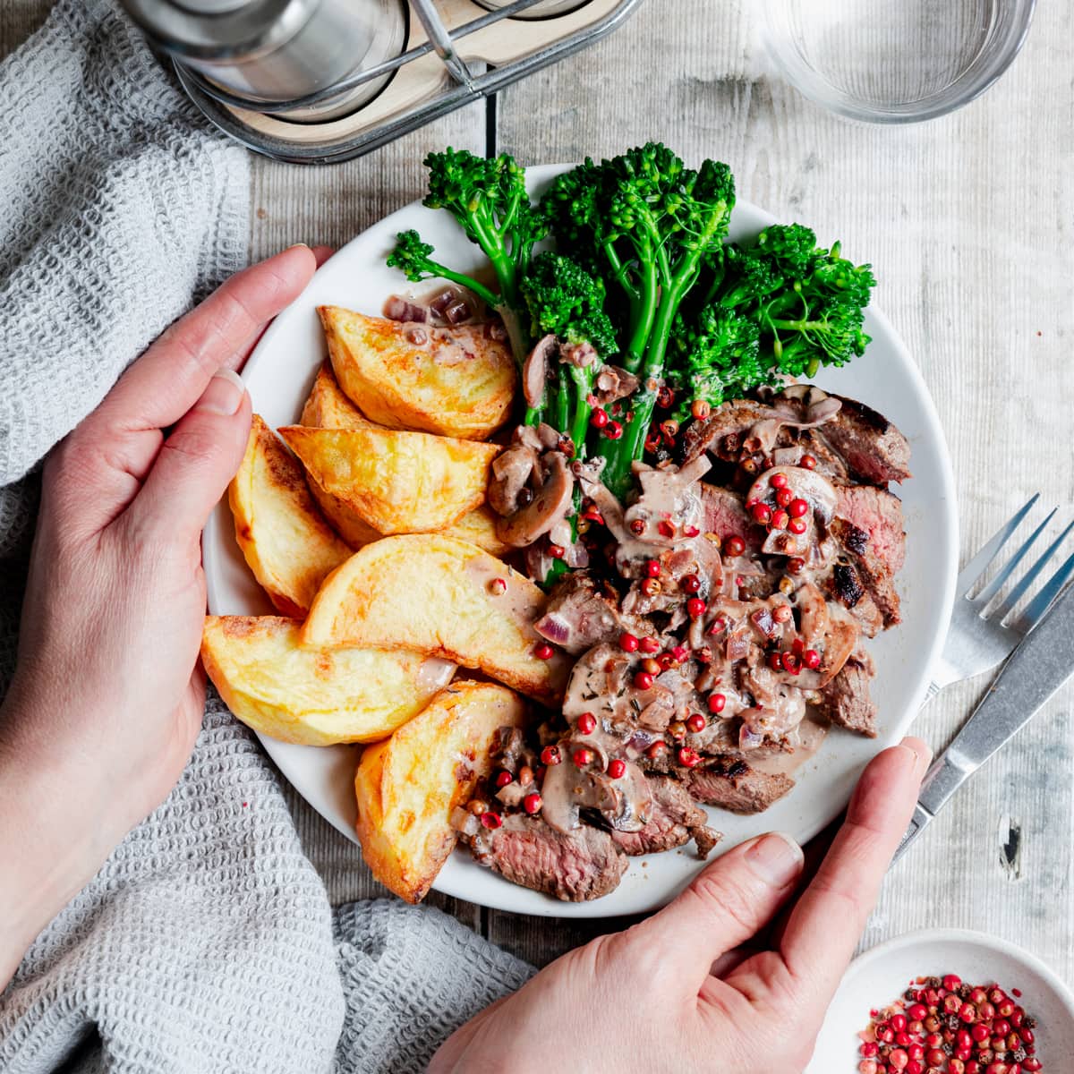 Plate of steak with potato wedges, broccoli and pink peppercorn sauce