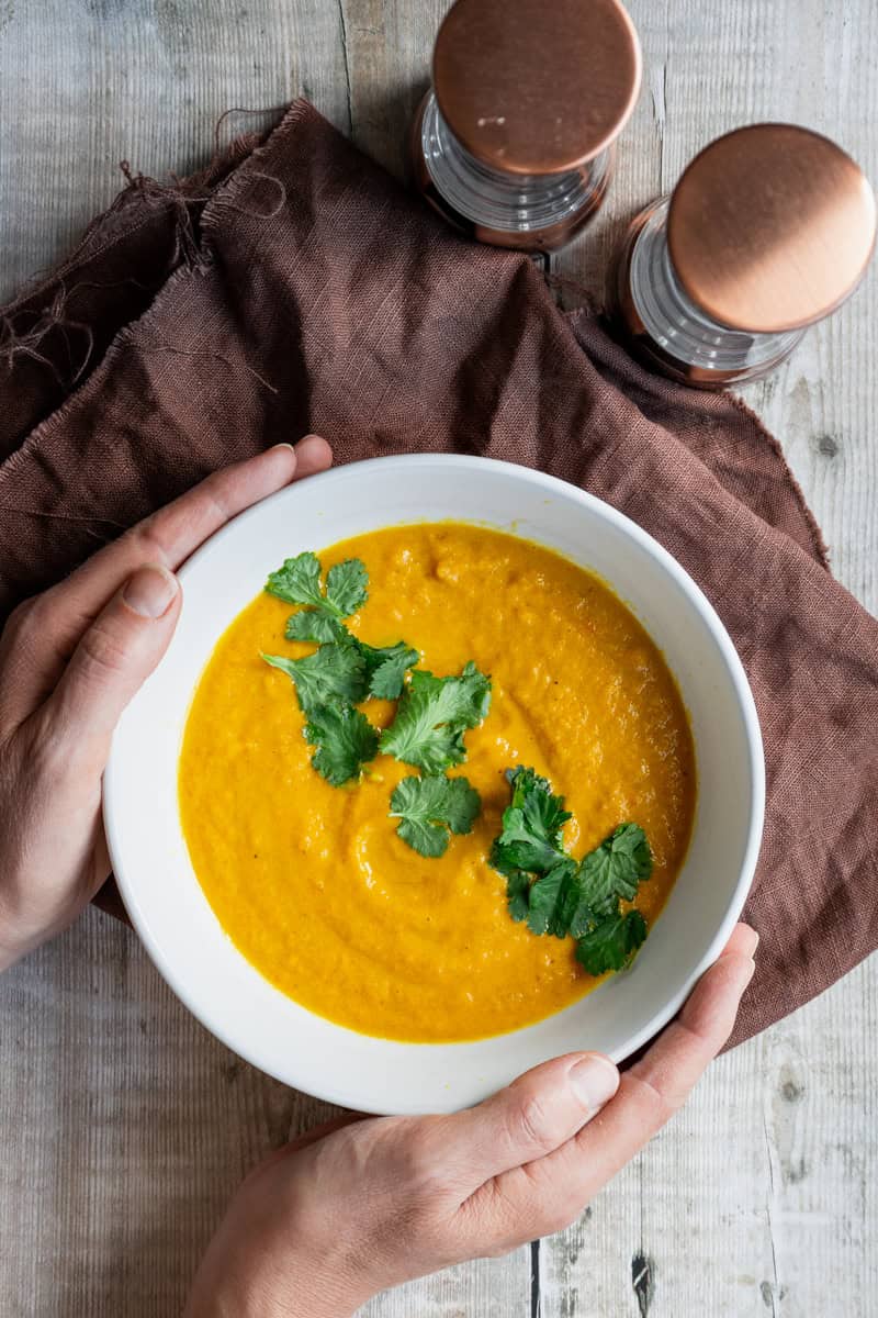 hands holding a bowl of carrot and tahini soup