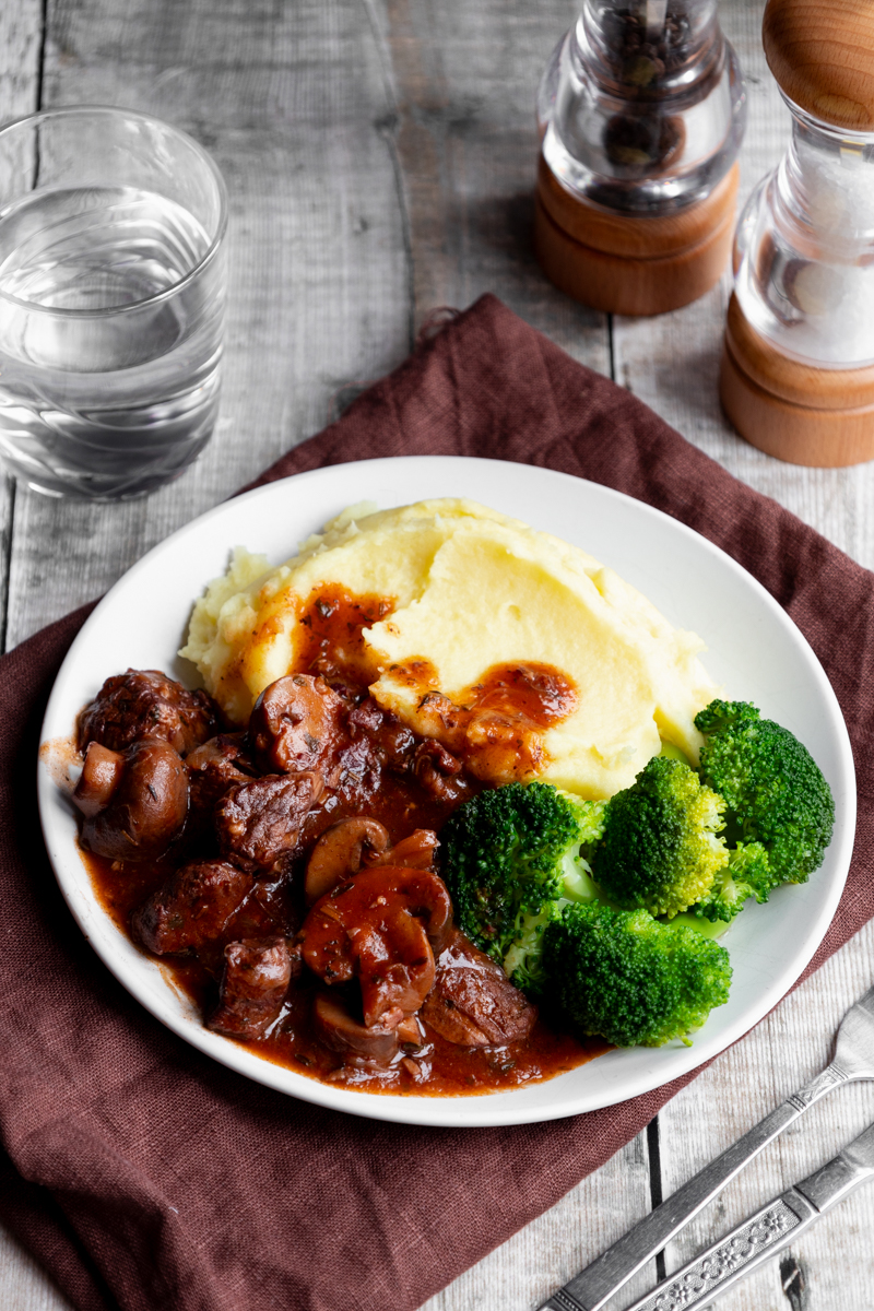 plate of rich beef bourguignon with sides of potato and broccoli