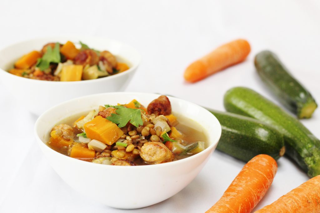 bowls of sausage lentil vegetable soup with carrots and courgettes in the background