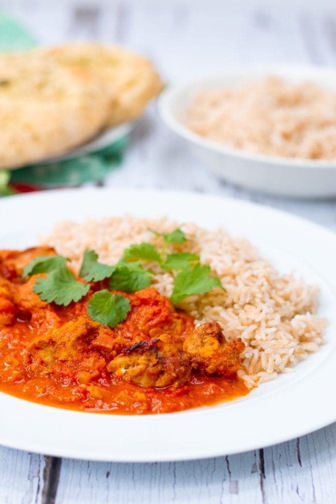 plate of chicken tikka masala rice rice and naan in the background