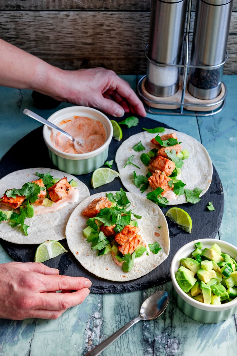 hands putting down a board of tandoori salmon tacos